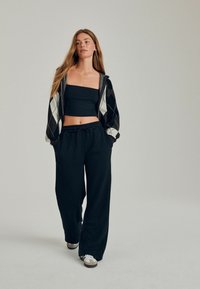 Černý zkrácený top, sako s vzorem argyle a černé široké kalhoty. Outfit má volný střih a lehkou látku. K dispozici jsou i tenisky.