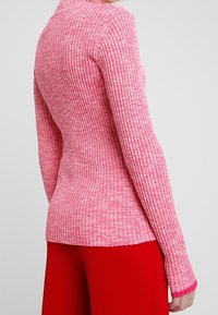 Rosa ribbad stickad tröja med hög krage, figursydd form, långa ärmar och kontrasterande rosa muddaccents. Strukturerad finish genom hela plagget.