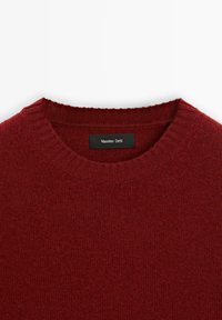 Červený pletený svetr s kulatým výstřihem a žebrovanými manžetami. Obsahuje tkanou nálepku s nápisem "Massimo Dutti" v bílé barvě na černém pozadí.