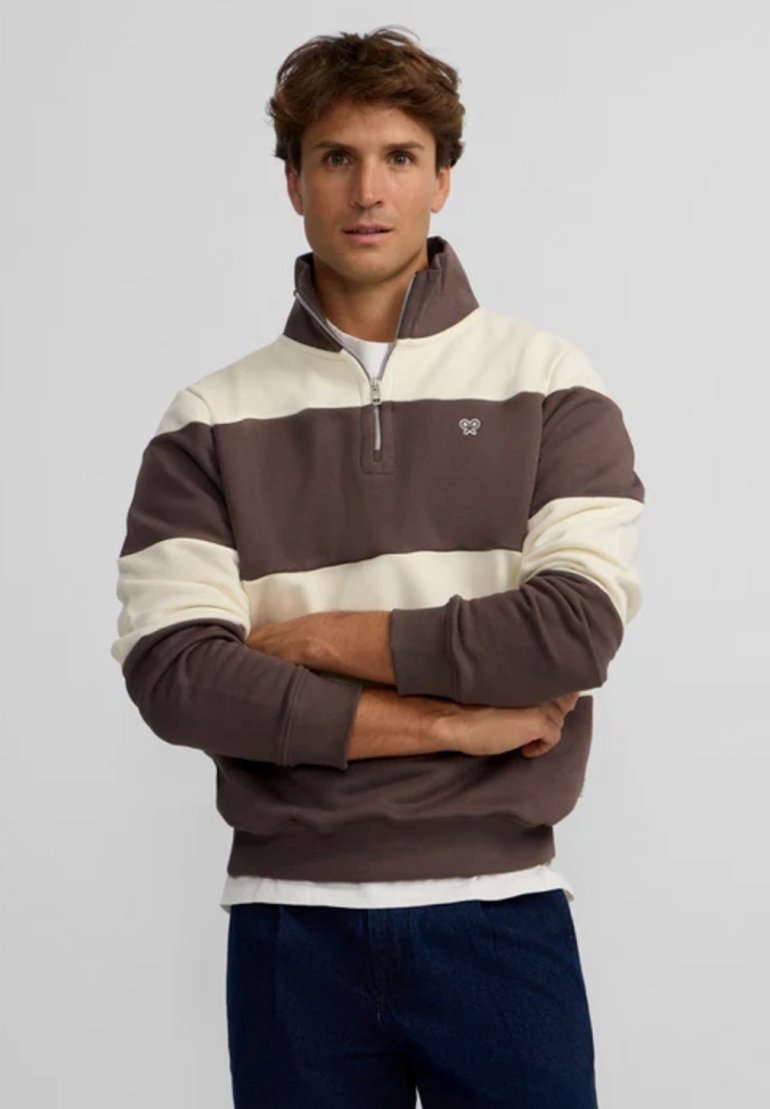Pull brown et crème à rayures avec un col zippé, fabriqué en tissu doux. Présente un petit logo sur la poitrine et des poignets côtelés.