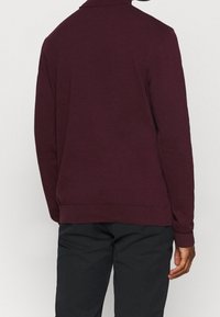 Bordowy sweter z wysokim kołnierzem, ściągaczami na mankietach i u dołu, wykonany z miękkiego materiału. Widok od tyłu pokazuje gładką fakturę bez widocznych wzorów.