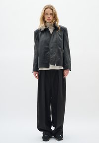 Giubbotto di pelle nera con chiusura a zip, spalle larghe e una vestibilità relax, abbinato a pantaloni neri larghi e un dolcevita leggero.