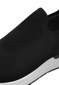 Scarpa nera in maglia slip-on con superficie testurizzata, dettagli a coste e suola bianca a contrasto con un motivo testurizzato.