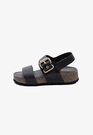 Sandalia de cuero negro texturizado con dos correas, hebilla dorada, suela plataforma de corcho y correa de talón ajustable, vista lateral sobre fondo blanco.