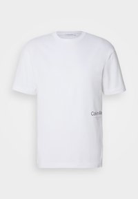 Biała bawełniana koszulka z krótkim rękawem, okrągłym dekoltem i czarnym logo Calvin Klein nadrukowanym na dolnej lewej stronie. Gładka tekstura.