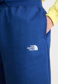 Μπλε φόρμες από μαλακό ύφασμα, με επενδεδυμένο λευκό λογότυπο "The North Face" στο αριστερό πόδι και ελαστική μέση.