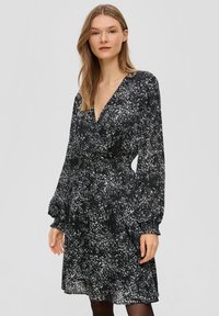 Schwarz-weißer gemusterter Kleid mit tiefem V-Ausschnitt, langen Ballonärmeln und taillierter Taille. Leichter, fließender Stoff mit strukturierter Oberfläche.