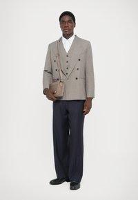 Szürke, dupla gombolású blézer fehér ing felett, csíkos navy nadrággal párosítva, és egy kis bézs válltáskával. Fekete cipő is tartozik hozzá.