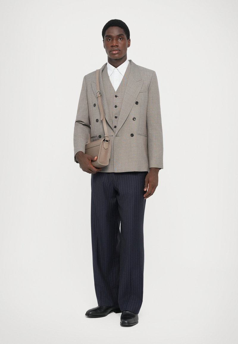 Grau doppeltbreasted Blazer über einem weißen Hemd, kombiniert mit navy-blauen gestreiften Hosen und einer kleinen beigen Schultertasche. Schwarze Schuhe inklusive.