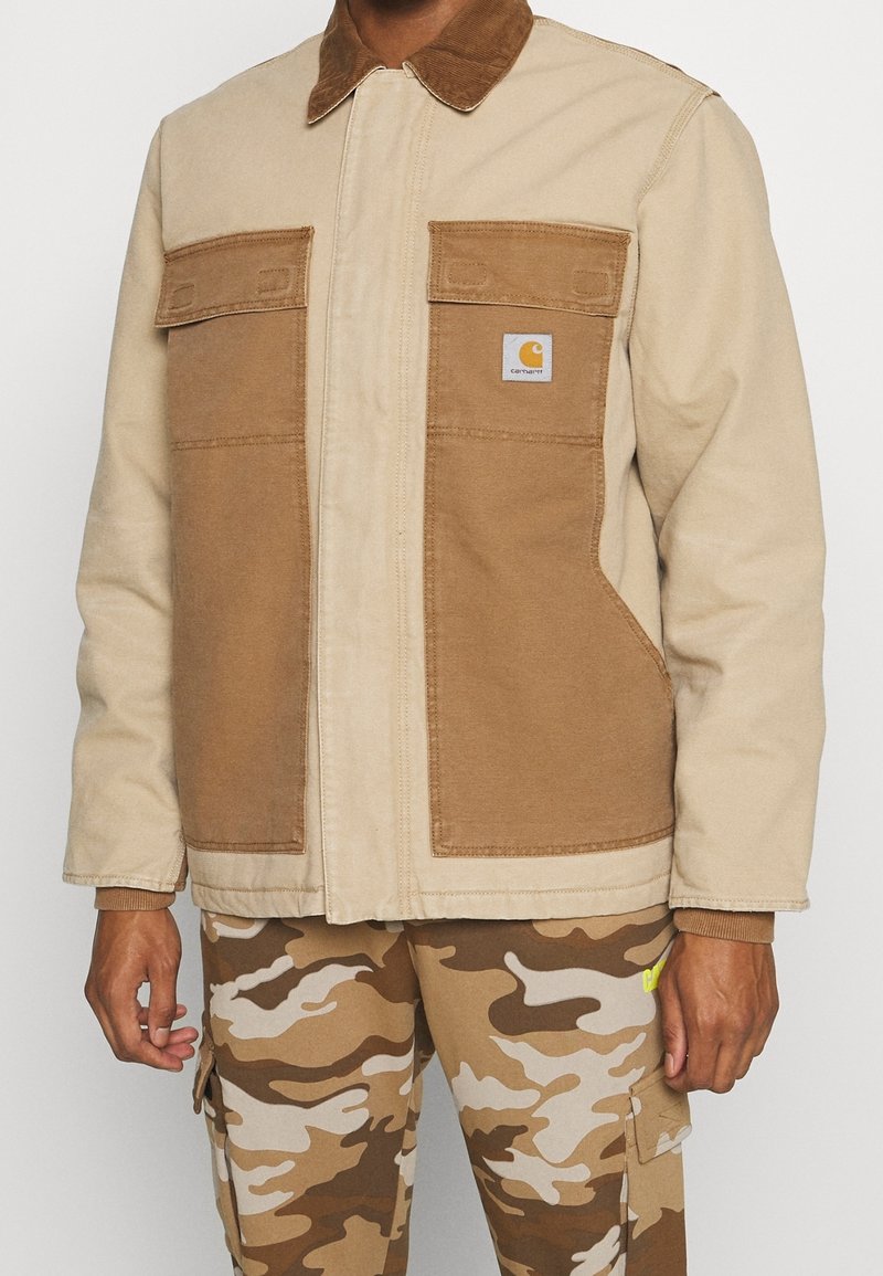 Man met een beige en bruine color-block jack met zijzakken en tan camouflage cargobroek.