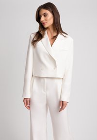 Biały krótki żakiet z podwójnymi guzikami i jedną kieszenią, sparowany z szerokimi spodniami w tym samym kolorze. Gładki materiał, dobrze dopasowany krój.