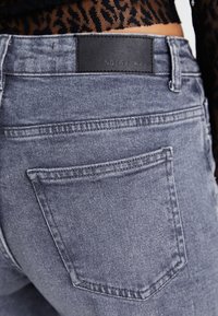 Denimjeans i blekt grått med en texturerad yta. Har en svart läderlabel i midjan och standard bakfickor.