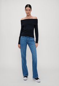 Svart off-the-shoulder topp med lange ermer, kombinert med lyseblå straight-leg jeans og svarte joggesko med hvite såler.