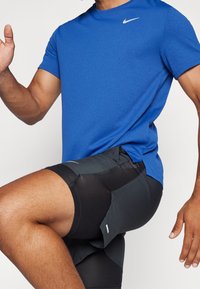 Camiseta deportiva azul de manga corta con cuello redondo y logotipo de Nike, combinada con pantalones cortos negros con estampado, bolsillos laterales y paneles texturizados.