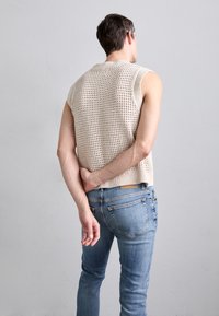 Beige stickad ärmlös tröja med öppen sömnad, i kombination med ljusblå jeans med medelhög midja och klassisk femfickorsdesign.