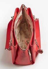 Czerwona skórzana torebka z zamkiem błyskawicznym na górze, z beżowym wnętrzem z powtarzającym się wzorem logo oraz bocznymi kieszeniami na zamek.