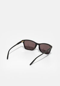 Óculos de sol de plástico preto com lentes cinzentas escuras, apresentando um design elegante e angular, com discretos detalhes em dourado nas dobradiças.