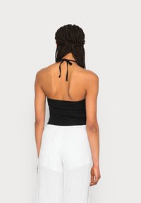 Top halter preto com corpete ajustado, combinado com calças largas e fluidas brancas. O top apresenta uma alça amarrada no pescoço. Texturas suaves em toda a peça.