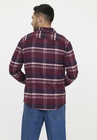 Chemise en flanelle à carreaux rouges et marine avec un col boutonné, comportant un empiècement au dos et des détails de marque subtils au niveau du col.