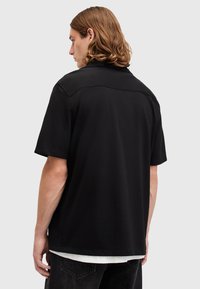 Black short-sleeve shirt with a collar, featuring a smooth texture and a relaxed fit. Back view shows flat stitching and a minimalist design.