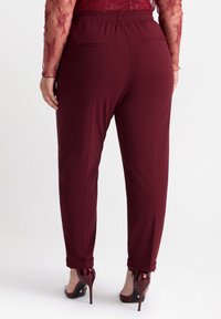 Burgundybyxor med elastisk midja och uppvikt fåll, tillverkade av ett mjukt tyg, med två bakfickor och en skräddarsydd passform.
