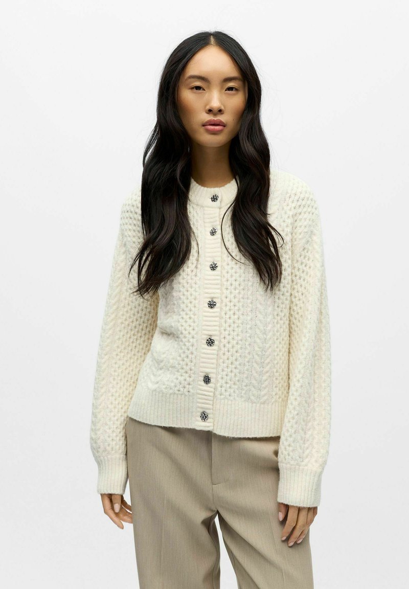 Kreemikas kudumiga kardigan, mis on tekstuurse mustriga, soonikkoes varrukaservade ja kangast kaetud nuppudega ees. Hele ja hubane välimus.