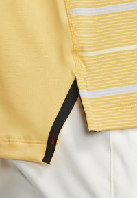 Žluté sportovní tričko Nike s vodorovnými bílými pruhy, černými bočními akcenty a malým červeným logem poblíž lemu, vyrobené z prodyšného materiálu.