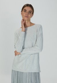 Helles graues Langarmshirt mit einem Bootsausschnitt und gerippten Bündchen, das eine weiche Textur und eine lockere Passform aufweist, kombiniert mit einem metallischen Rock.