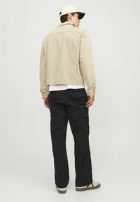 Jachetă din denim bej, pantaloni cargo negri, adidași crema. Design casual, cusături vizibile și buzunare pe pantaloni. Croială structurată, lejeră.