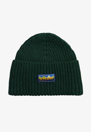 Bonnet en tricot ribbé vert avec un revers, orné d'un patch rectangulaire bleu avec du texte jaune. La texture semble douce et extensible.