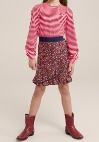 Červené a bílé pruhované triko s dlouhým rukávem spárované s tmavě květinovou sukní s volánky. Modelka má na sobě červené kovbojské boty.