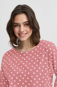 Heled roosa pullover-särk, millel on valged täpid, laia dekolteega ja lõdva istuvusega. Valmistatud pehmest kangast sileda tekstuuriga.