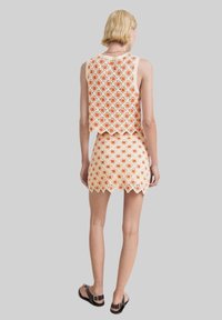 Háčkovaná dvoudílná souprava se topem bez rukávů a mini sukní. Vyrobena z krémové příze s oranžovými květinovými vzory a vroubkovanými okraji.