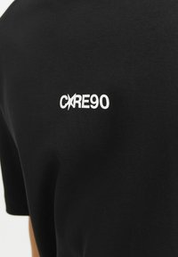 Sort bomulds T-shirt med rund halsudskæring og korte ærmer. På ryggen står der hvid tekst med teksten "CXRE90" i en moderne skrifttype.