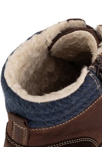 Pruuni nahast saabas, millel on sinine villane krae ja kreemjas fleece vooder. Omab tikandiga disaini ja taga on tõmbeaas mugavaks selga panemiseks.