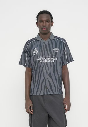 Polo a manica corta grigia con strisce zebrate nere. Presenta un colletto e dettagli in testo bianco. Realizzata in tessuto leggero.