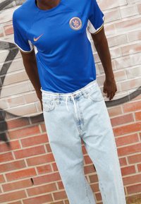 Camiseta azul de Nike con cuello redondo, acentos blancos y un logo, combinada con jeans rectos de color azul claro que muestran una textura desgastada.