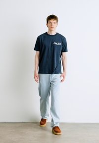 Marineblauwe katoenen t-shirt met "New York" print, gecombineerd met lichtblauwe denim jeans en bruine suède schoenen. Eenvoudige, casual fit.