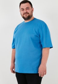 Modrá krátkohlavová tričko vyrobené z mäkkého bavlneného materiálu, s voľným strihom a dizajnom okrúhleho výstrihu, s rovnomerným šitím a bez viditeľných vzorov.