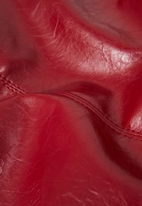 Rotes Leder mit glänzender Oberfläche, das subtile Falten und Texturvariationen aufweist. Steppnähte sind im oberen Bereich sichtbar.