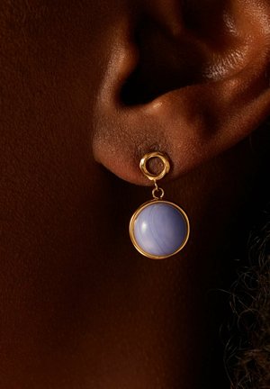 Boucles d'oreilles en or avec une pierre ronde, bleu clair, pendantes sous l'oreille. Texture lisse avec une finition polie.