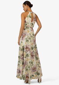 Robe longue à fleurs avec un dos en trou de serrure, ornée de grandes fleurs violettes et jaunes sur un fond clair, fabriquée en tissu léger.