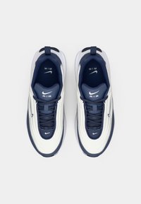 Bijele i tamnoplave tenisice s valovitom dizajnom, teksturiranim gornjim dijelom, vezanjem i vidljivim Nike logotipom s strane i na jeziku.