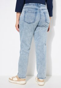 Vaqueros de mezclilla azul claro con un corte relajado, waistband elástico y dos bolsillos traseros. Tejido texturizado con un desvanecimiento sutil, combinados con zapatillas beige.