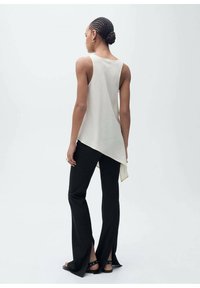 Asymmetrical cream tank top made of smooth fabric, paired with black flared pants featuring slits at the hem and simple black sandals.