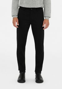 Pantalones negros de corte ajustado, con cierre de botón, passadores para cinturón y una textura suave. Combinados con botines negros.