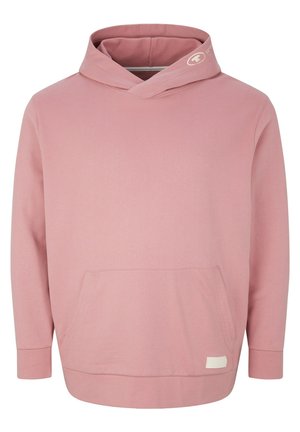 Homme portant un sweat à capuche rose avec poche kangourou, jean bleu clair retroussé et baskets blanches, debout contre un fond blanc.