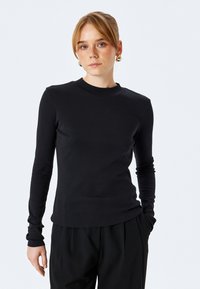 Czarny longsleeve z długim rękawem, prążkowana tekstura, okrągły dekolt, dopasowany krój, w zestawie z luźnymi czarnymi spodniami. Brak widocznych wzorów lub logo.