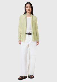 Cardigan verde chiaro con maniche lunghe, apertura frontale e tessuto testurizzato, abbinato a pantaloni bianchi a gamba larga e sandali neri.