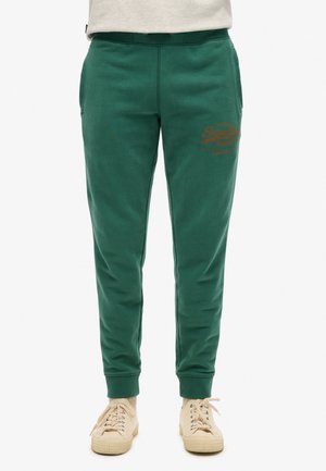 Groene trainingsbroek met elastische tailleband, zijzakken en een logo in bruin op de bovenbeen. Zachte katoenen stofmix.